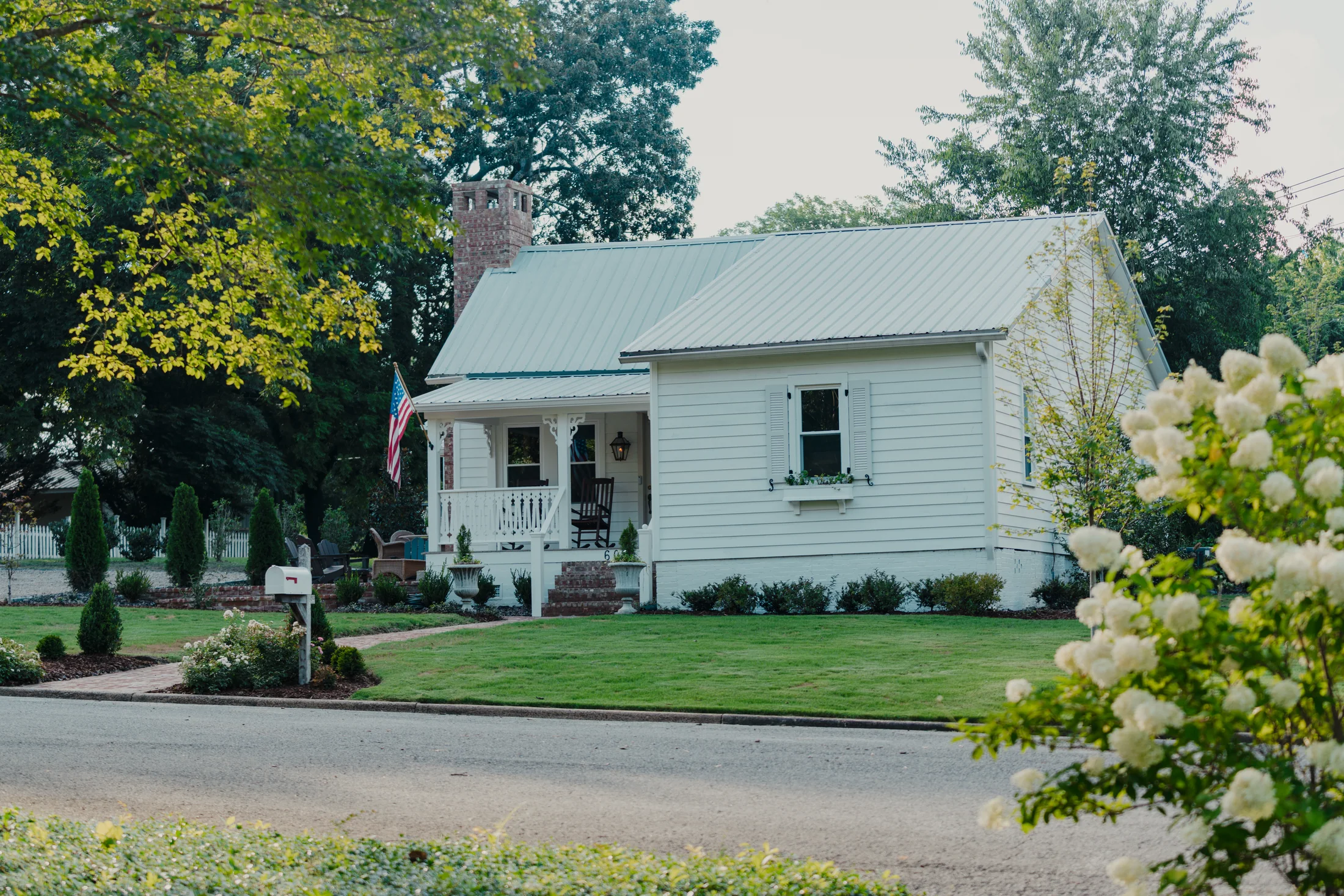 White cottage with a front porch, garden and mature trees