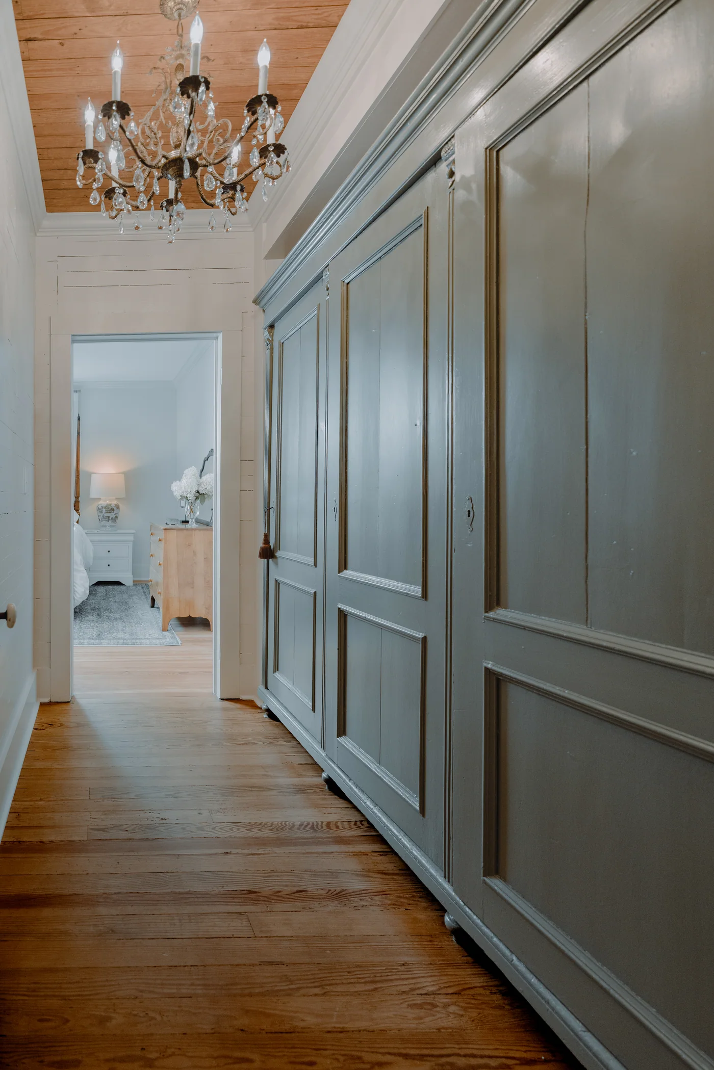 Architectural hallway with a chandelier, wood floors and pale blue paneled storage