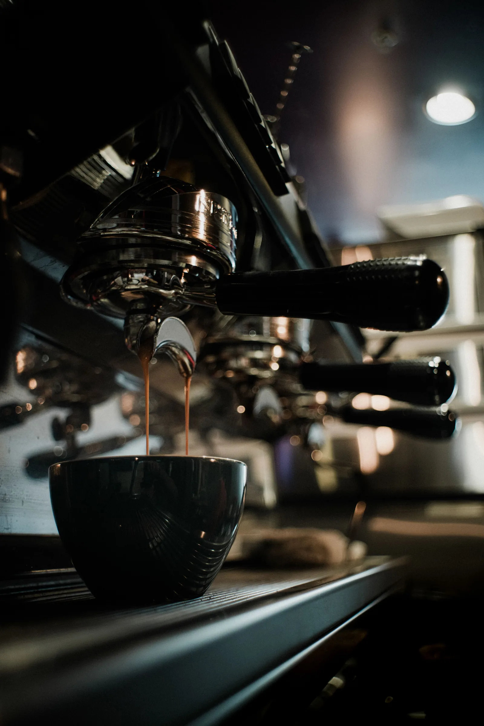 Espresso pouring from a cafe machine into a dark ceramic cup