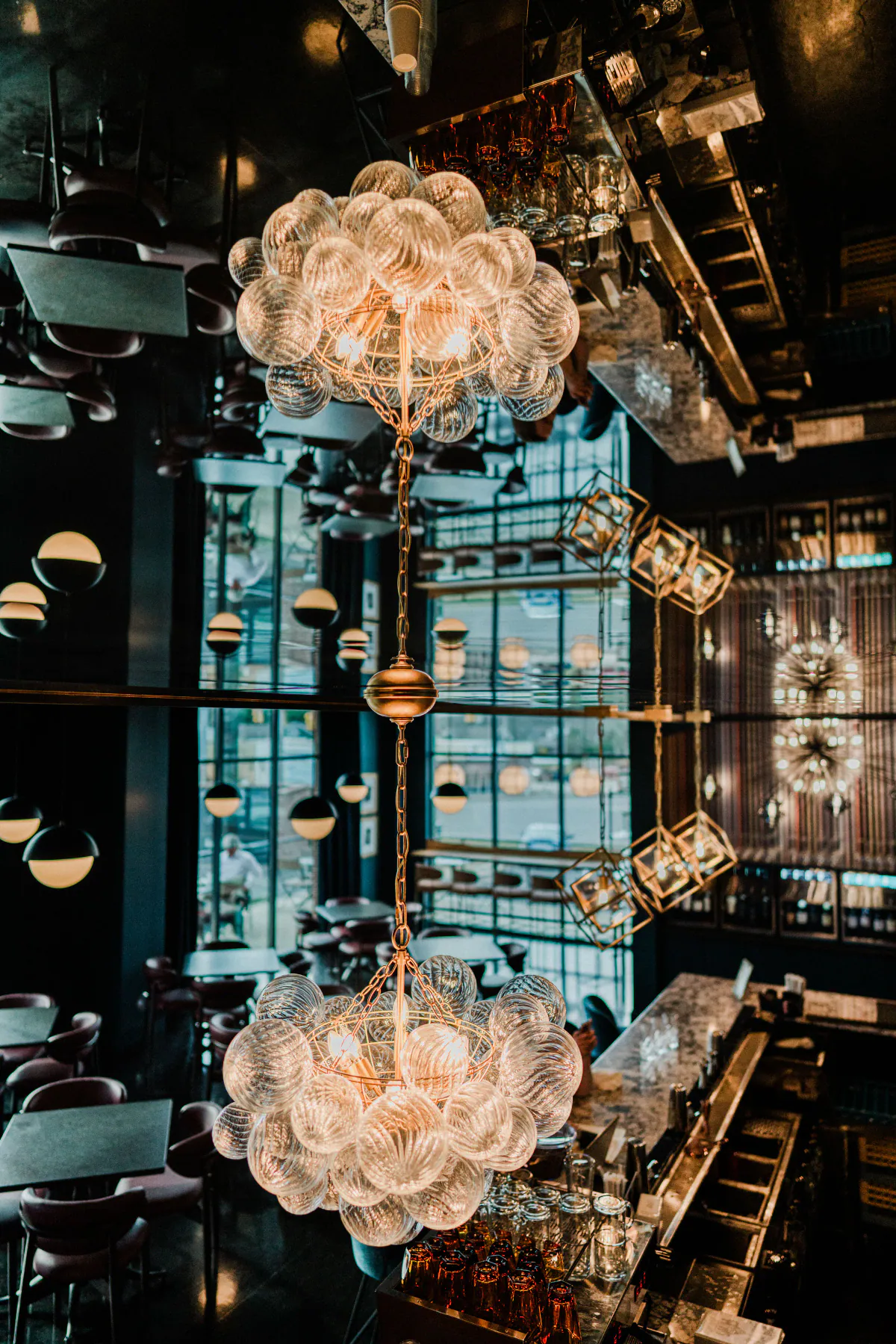 A dramatic mirrored bar interior with sculptural glass lighting photographed by Jacob Fine